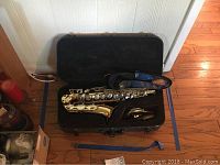 Full view of Evette saxophone inside black hard case with blue strap and mouthpiece visible
