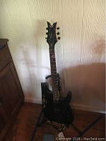 Full view of electric guitar on stand, showing the black body, strap, and floor surface.