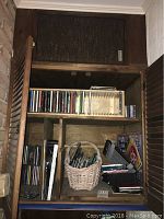 Wooden shelving unit holding multiple CDs, a woven basket with miscellaneous items, and some posters, showing storage of lot contents.
