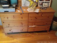 Photo of the wooden dresser with six drawers and some items on top, showing the front view and wooden construction with round knobs.