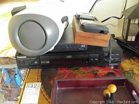 Panasonic BluRay player with a white Canon camera on top and other small electronics and accessories visible on a floral table.