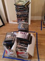 Photo showing multiple stacks of DVDs piled on floor and inside bags. Cases show warping and moisture damage signs.