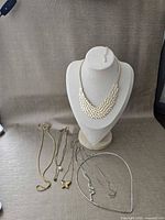 Group shot showing all eight necklaces laid out with bib on display bust