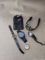 All five watches and key pouch arranged on fabric backdrop