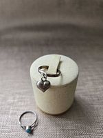 Both rings displayed; heart charm ring on stand, turquoise ring foreground