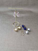 Front view of all five earring pairs on fabric background and stand
