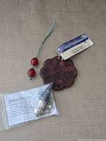 Full lot showing pendulum pendant in sleeve, carved floral pendant with tag, two red beads on green cord