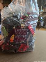Front view of clear bag filled with mixed LEGO pieces, visible minifigure, wheels, bricks