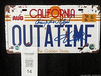 Front view of signed OUTATIME licence plate with MaxSold tag