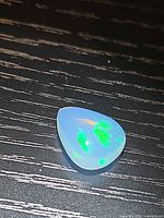 Pear-shape opal on dark surface showing green flashes