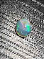 Oval opal on textured black surface showing multicolor play-of-color
