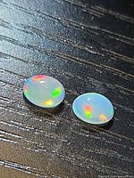 Two translucent opal cabochons on dark surface showing play of colour
