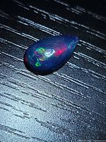 Pear-shaped black opal showing multicolour play on dark surface