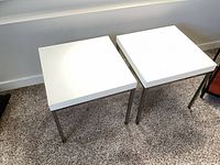 Pair of tables showing white laminate tops and metal legs
