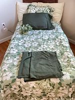 Twin bed dressed with floral comforter, sham, pillowcase, sheets and faux potted greenery visible