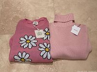 Allude turtleneck and Willow Paige daisy sweaters folded with tags visible
