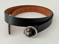 Full belt coiled showing exterior black leather, tan interior and silver buckle
