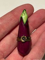 Porcelain eggplant pill box in hand showing scale, brass flower clasp visible