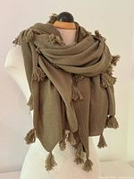 Full view of shawl draped on mannequin showing olive color and tassels