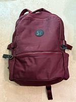 Front view of burgundy Lululemon backpack showing logo, pockets and straps