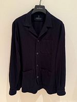 Front view of dark blue pinstripe wool shirt jacket on hanger, showing collar, buttons, pockets, sleeves