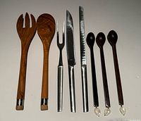 All eight utensils laid out: rosewood spoons, Austrian stainless carving set, Bérard teak servers