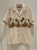 Front view of cream Hawaiian shirt on hanger, showing ukulele, palm tree and floral print