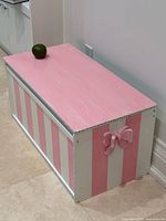 Wooden toy chest painted pink and white stripes, top view with apple for scale