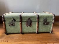 Full front view of green canvas trunk showing wood slats and hardware