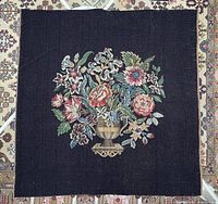 Full view of square floral needlepoint tapestry on patterned rug