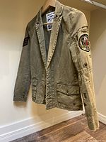 Full front view of khaki cotton jacket on hanger showing overall style and condition