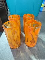 Four orange swirl glass tumblers on wooden surface
