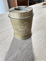 Full view of cylindrical brass ashtray showing rim slot and arrow engravings