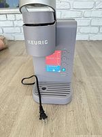 Front view of gray Keurig coffee maker with cord and drip tray visible