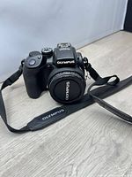 Front view of Olympus SP-570UZ camera with lens cap and strap