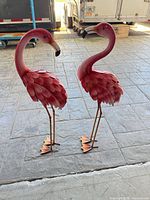 Full view of both metal flamingo sculptures standing side by side