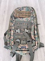 Front view showing digital camo pattern, MOLLE webbing, buckles