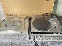 Both turntables side by side under dust covers; Technics on right with platter and mat, JVC on left missing platter