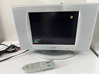 Front view of Sharp 13" LCD TV displaying channel number, remote and cables visible