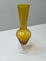 Full view of amber glass vase on clear pedestal