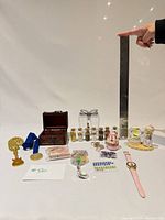 Overview of entire lot with ruler for scale, showing trinket box, vials, ornaments, medals, rhinestones, watch and figurine