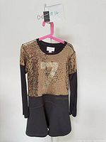 Front view showing gold sequin bodice, black knit sleeves and skirt, numeral 7, hanger and tag visible