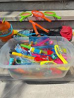 Clear bin filled with assorted bubble wands, paddles, small toys; racquets and boomerang on step