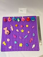 Overview of all squishy toys arranged on purple pop-it mat with ruler for scale