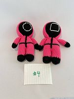 Front view of both crochet plush dolls showing mask emblems
