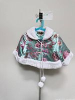 Front view of aqua satin brocade toddler cape on hanger showing faux fur collar, hem and pom-pom ties