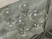 Four clear glass dessert coupes on glass surface
