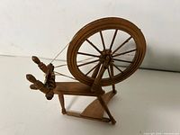 Left-front view of miniature wooden spinning wheel showing drive wheel, treadle and spindle
