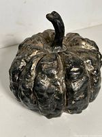 Front angled view of cast metal pumpkin showing distressed black and gold finish