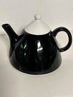 Full view of black ceramic teapot with white lid showing handle and spout